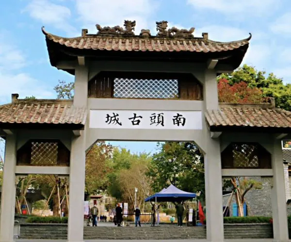 Nantou Ancient City,Shenzhen,Chinatravel Traditional Chinese-style gateway with a tiled, up-curved roof and decorative dragons on top, opening to a courtyard and trees; sign displays four Chinese characters above the entrance (the gate to Nan Tou Ancient Town).