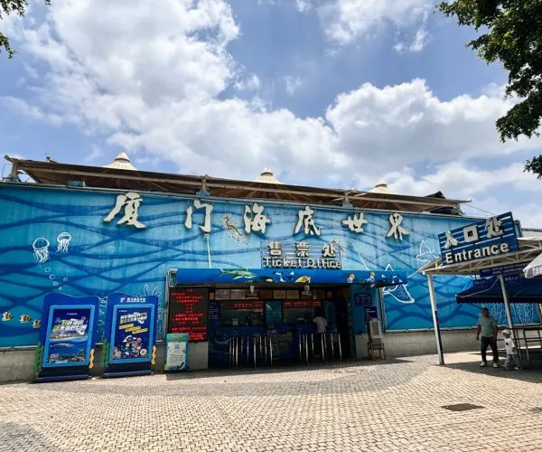 Xiamen Underwater World,Xiamen,Chinatravel Blue exterior wall with ocean-themed artwork and large white Chinese characters; ticket office and entrance signs visible in front of an aquarium or marine park.