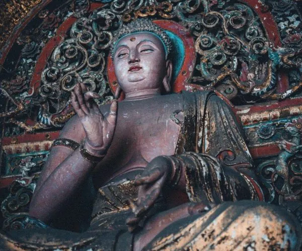 Shuanglin Temple,Pingyao,Chinatravel Seated Buddha statue in an ornate shrine with intricate red and gold carvings, one hand raised in blessing (temple context)