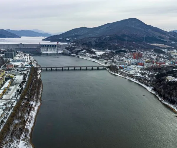 Jilin City,Jilin,Chinatrip Aerial winter view of a dam across a wide river with a town and hills in the background.