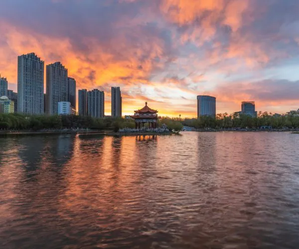 Hohhot Weather,Hohhot,Chinatrip Sunset over a city skyline with a traditional Chinese pavilion on an island in the foreground.