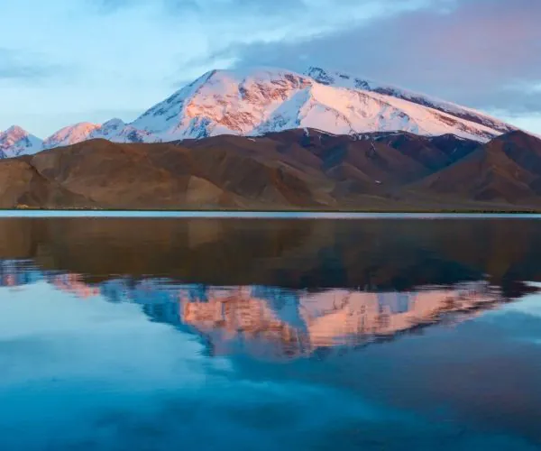 Karakul Lake,Kashgar,China tour Snow-covered mountain range bathed in pink twilight, reflected in a calm lake below.