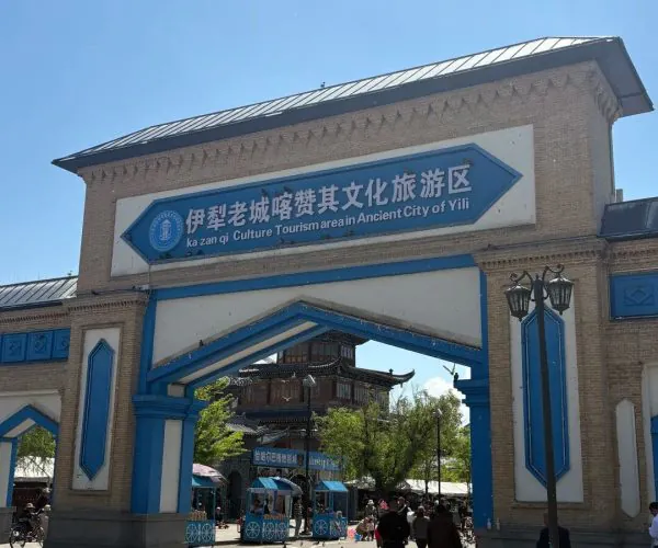 Kazanqi,Ili ,China tour Blue-and-white arch gateway marking a culture tourism area; sign in Chinese, pedestrians pass beneath as a traditional building is visible beyond the opening