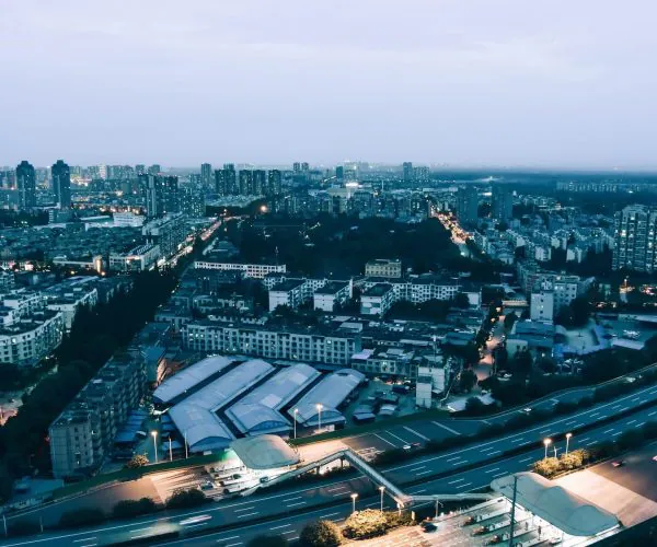 Sichuan,Chinatravel Aerial view of a sprawling city at dusk, with a curving highway in the foreground and dense apartment blocks beyond.