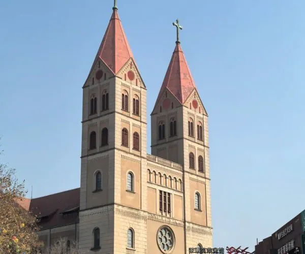 St. Michael’s Cathedral,Qingdao,Chinatravel Twin-towered church with red pitched roofs reaching toward a blue sky; stone facade and arched windows, with people walking nearby.
