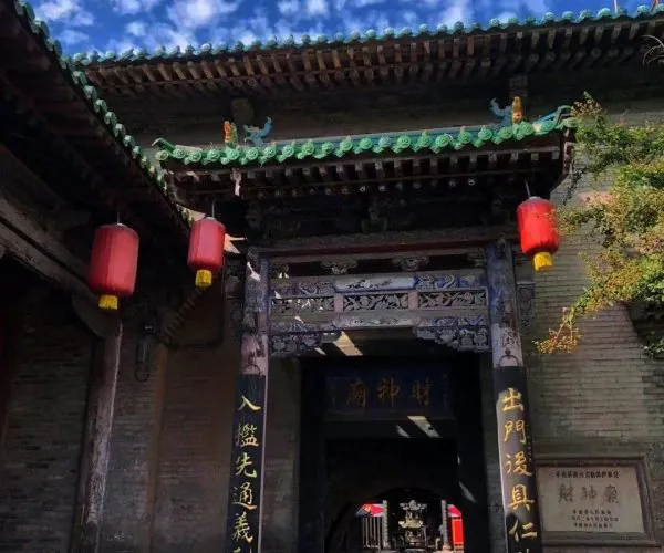 City God Temple,Pingyao,Chinatravel Ancient Chinese temple gate with ornate carved wood, green tiled roof, and red lanterns at the entrance.