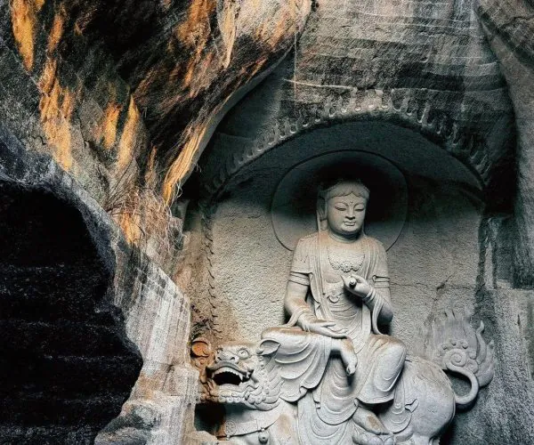 Great Buddha Temple,Shaoxing,Chinatravel Stone Buddha statue seated in a cave niche with a dragon at its base, carved from rock walls with warm light on the left edge.