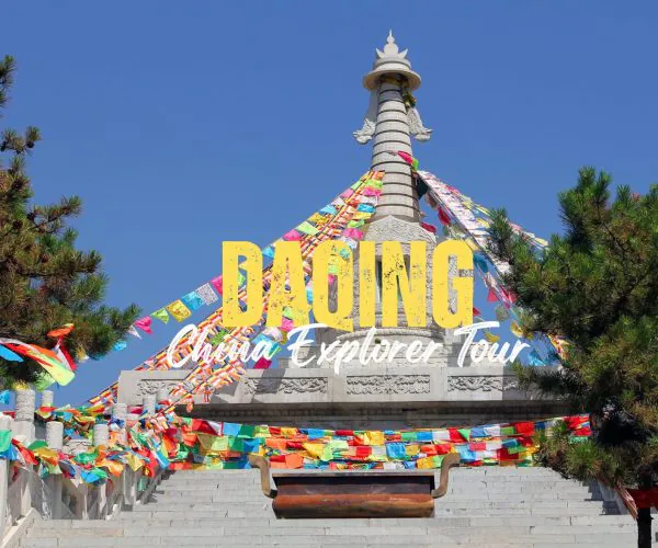 Daqing,Heilongjiang,Chinatravel Promotional travel image of a Buddhist stupa with multicolored prayer flags against a blue sky, bordered by stairs and trees.
