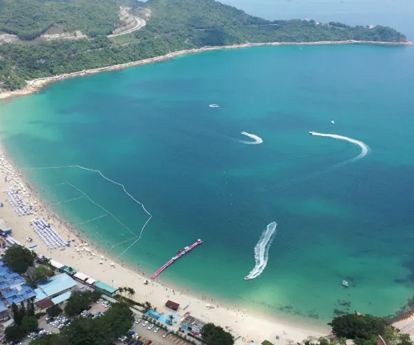 Dameisha & Xiaomeisha Beaches,Shenzhen,Chinatravel Aerial view of a turquoise bay with a sandy beach, sun loungers, and calm water encircled by green hills and buildings along the shore