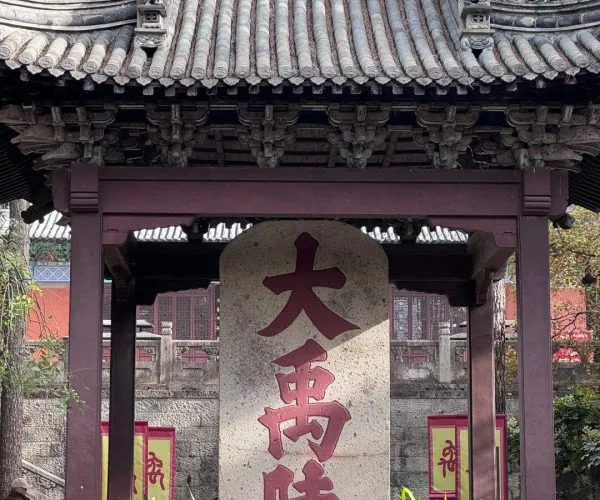 Dayu Mausoleum Scenic Area,Shaoxing,Chinatravel Traditional Chinese temple gate with a curved tiled roof and a tall stone tablet inscribed with large red Chinese characters in a courtyard setting.