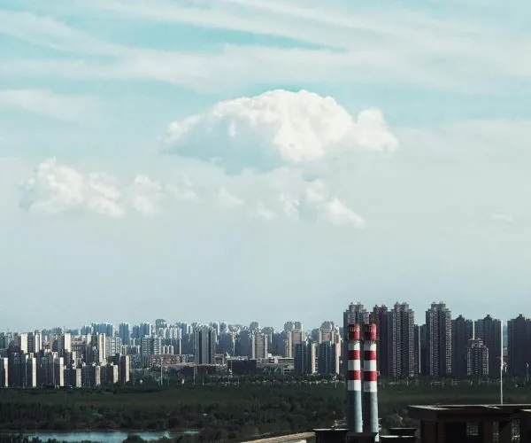 City skyline with numerous high-rise buildings and two red-and-white chimneys in the foreground against a clear blue sky,