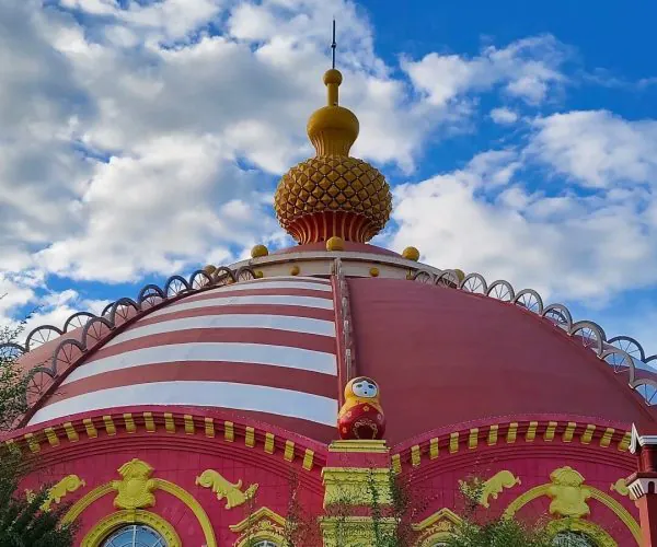Manzhouli Matryoshka Square,Hulunbuir,Chinatrip Colorful domed building with pink and yellow façade and a gold onion dome against a blue sky.