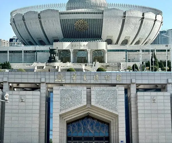 Ningxia Museum,Yinchuan,Chinatrip Wide shot of a futuristic museum with a silver, domed roof and tall curved exterior, flanked by staircases and a grand entrance.