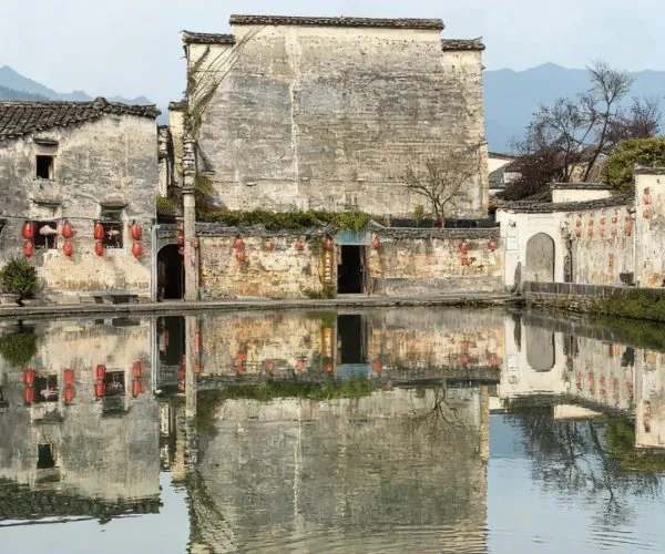 Hongcun & Xidi Villages,Huangshan,Chinatravel Historic gray-walled village with red lanterns along a waterside, reflected in a calm pond with distant mountains in the background