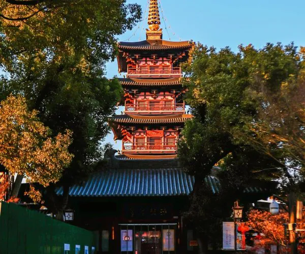 Hanshan Temple,Suzhou,Chinatravel Red multi-tier pagoda rising among green trees against a blue sky in a temple grounds scene.