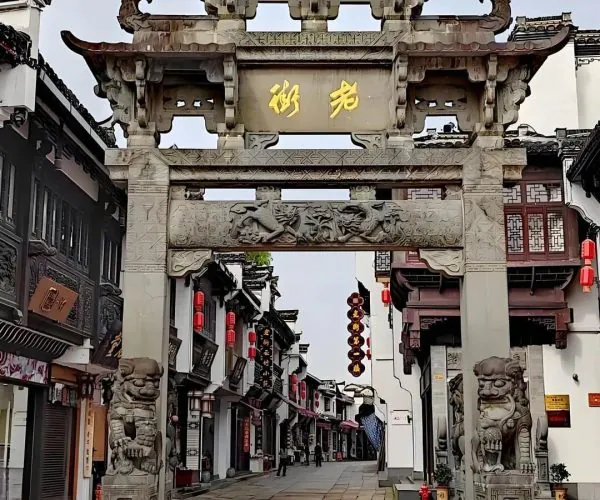 Tunxi Ancient Street,Huangshan,Chinatravel Stone ornate Chinese paifang gateway with dragon-headed ornaments and gold characters over a pedestrian shopping street lined with lanterns and traditional buildings.