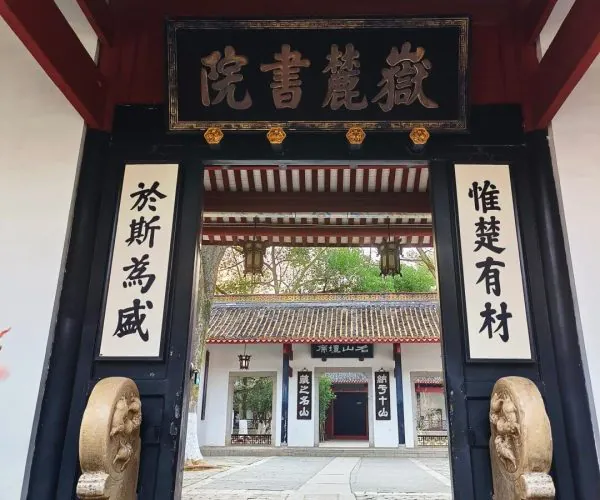 Yuelu Academy,Changsha,Chinatravel Temple entrance with red wooden beams and a black plaque with gold Chinese characters, flanked by vertical signboards and stone guardian statues, opening to a tiled courtyard.