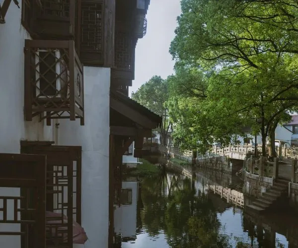 Pingjiang Road Historical Street,Suzhou,Chinatravel White-walled building with dark wooden lattice balconies beside a calm canal, trees reflected in the water.