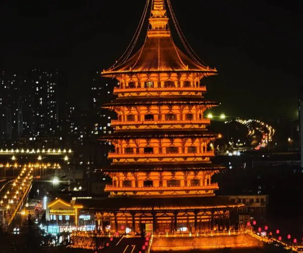 Yingtian Gate,Luoyang,Chinatravel Nighttime scene of a tall, orange-lit, multi-tiered Chinese pagoda with illuminated eaves in an urban setting
