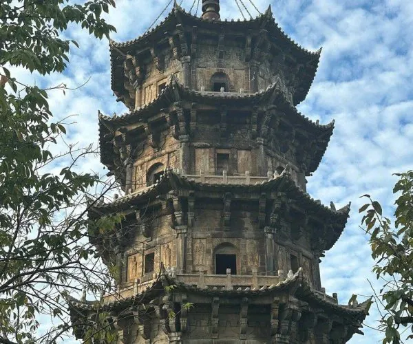 Kaiyuan Temple & West Street,Quanzhou,Chinatravel Stone multi-tier pagoda with ornate, upturned eaves rising above surrounding trees and a blue sky behind it.