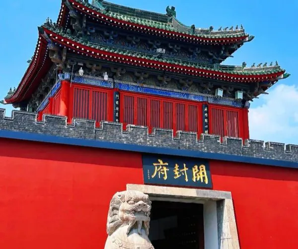 Kaifeng Mansion,Kaifeng,China tour Traditional Chinese temple gate with a ornate multi-tiered roof, red walls, and a stone guardian lion at the entrance beneath a gold plaque with Chinese characters.