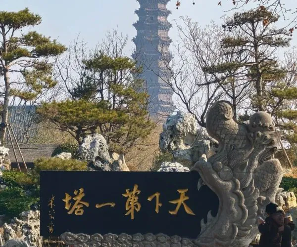 Kaifeng Iron Pagoda,Kaifeng,Chinatravel Stone dragon sculpture beside a black plaque with gold Chinese characters in a landscaped park, with a pagoda in the distance beyond the trees.