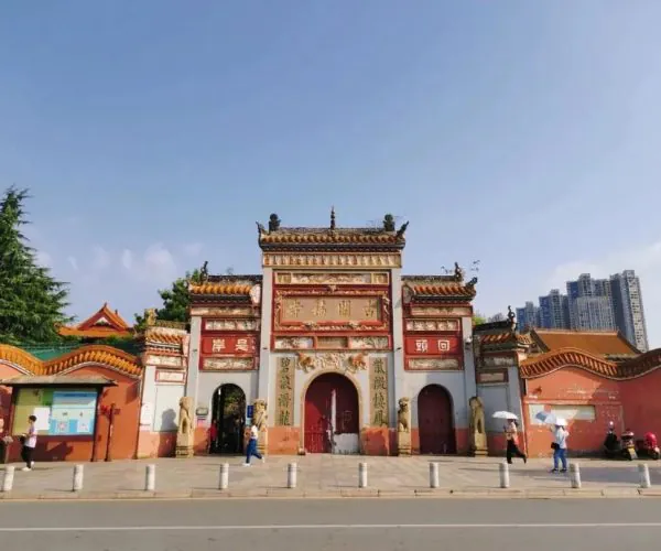 Kaifu Temple,Changsha,Chinatravel Traditional Chinese temple gate with red walls, ornate gold decorations, and three arches under a blue sky; people walking along a street in front.