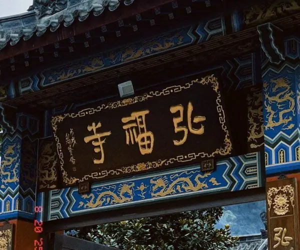 Hongfu Temple,Guiyang,Chinatrip Entrance to a traditional Chinese temple with a large black plaque bearing gold Chinese characters and intricate blue-gold decorative panels, plus a stone guardian lion statue nearby.
