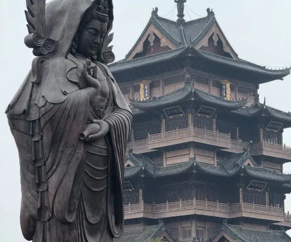 Guiyuan Buddhist Temple,Wuhan,Chinatravel Bronze statue of Guanyin with a flame-like halo beside a multi-tier Chinese pagoda temple in the background.