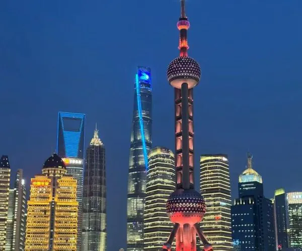 Night view of Shanghai skyline at dusk with the illuminated Oriental Pearl Tower by the river and modern skyscrapers nearby.