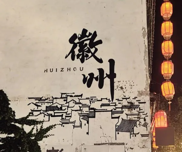 Huizhou Ancient City,Huangshan,Chinatravel A white wall with bold black Chinese characters reading '徽州' and a simple line drawing of a town below, illuminated by orange lanterns on the right at night.