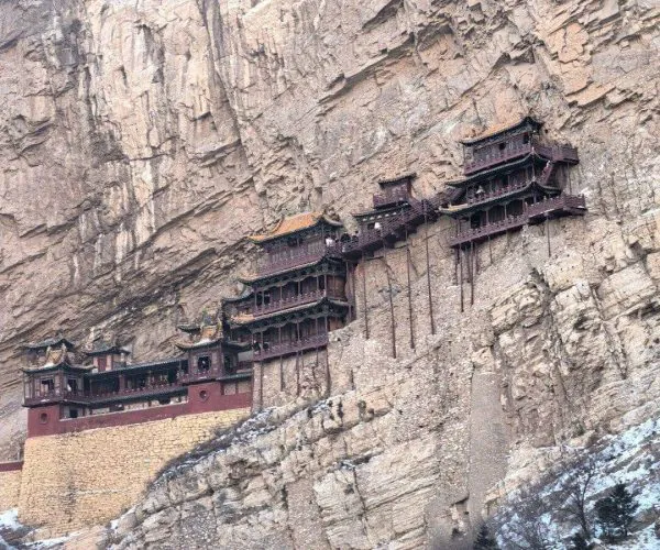 Hengshan Hanging Temple,Datong,Chinatravel Stone cliff with a multi-tiered Chinese pagoda complex built into the rock face, featuring red roofs and wooden balconies.","Traditional Chinese temple complex clinging to a sheer rock wall, several connected tiered pavilions with dark wood detailing.","Cliffside pagodas: a historic wooden temple structure mounted on a rocky mountainside, with snow at the base.","A series of connected temple pavilions attached to a rugged cliff, showcasing Chinese architectural style.","Rocky mountainside houses a layered temple complex, red-brown timber buildings perched along the cliff."