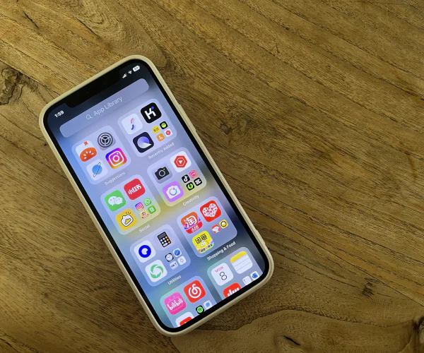 How To Stay Connected In China 2025: Internet, VPN And SIM Cards, chinaexplorertour, Smartphone with a grid of colorful app icons on a wooden table surface, seen at an angle.