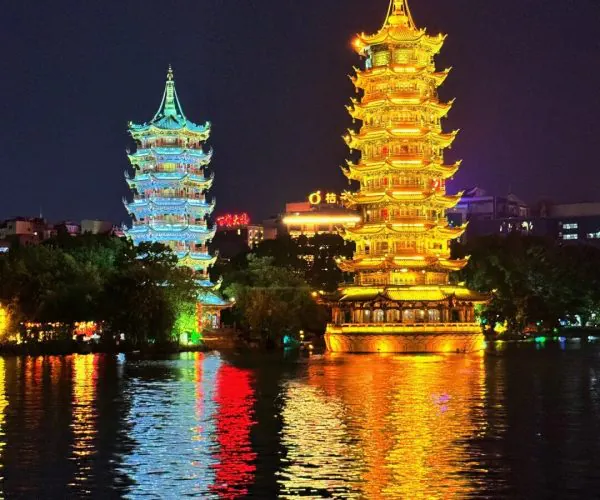 Sun and Moon Twin Pagodas,Guilin,Chinatravel Night scene of two illuminated pagodas by a lake, reflections dancing on the water (golden tower on the right, blue tower on the left).