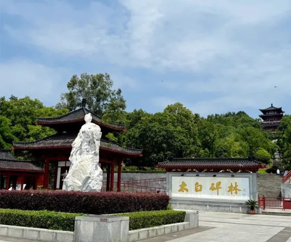 Li Bai's Former Residence,Mianyang,Chinatravel White stone statue in a Chinese temple courtyard with red pavilions behind, and a stone sign with gold Chinese characters under a blue sky.
