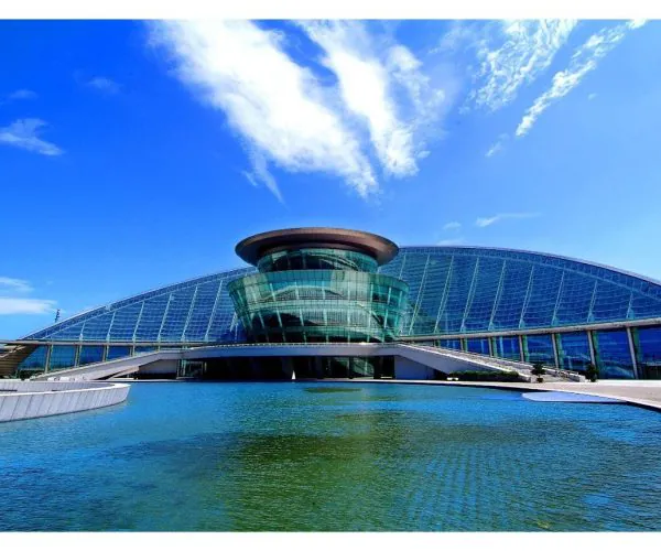 Hangzhou Grand Theatre,Hangzhou,Chinatravel Futuristic glass building with a circular glass tower, set beside a reflective pool under a blue sky.