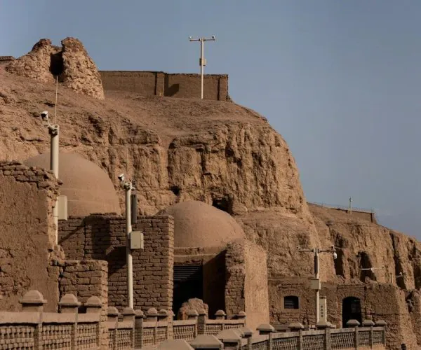Bezeklik Thousand Buddha Caves,Turpan,China tour Cliffside desert fortress with mud-brick walls, domed rooms, and a railing along the walkway edge.