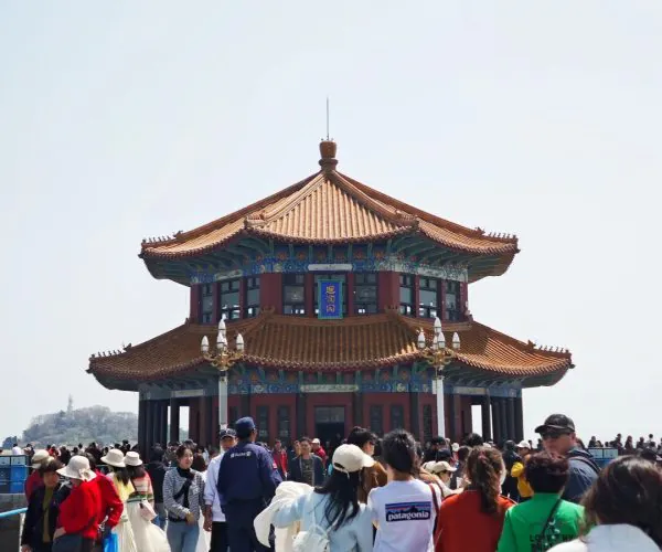 Zhanqiao Pier & Huilan Pavilion,Qingdao,Chinatravel Traditional multi-tiered pagoda with an orange tile roof and blue decorative trim, surrounded by tourists on a sunny day.