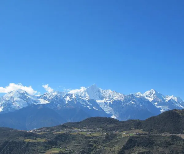 Meili Snow Mountain,Shangri-La,Chinatravel Snow-capped mountain range under a clear blue sky with a green valley and small village in the foreground.