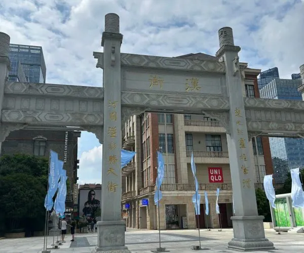 Han Street Pedestrian Zone,Wuhan,Chinatravel Granite traditional Chinese archway in a modern city plaza, gold inscriptions on the lintel, with blue banners and tall buildings in the background.