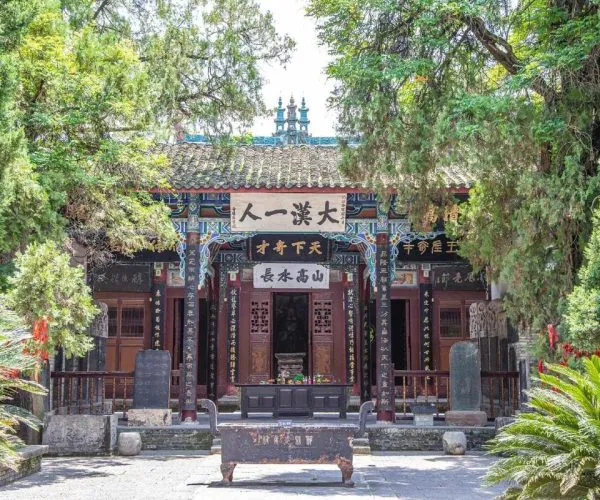 Wuhou Shrine, Chengdu, Chinatravel, Temple gate with ornate wooden pillars and Chinese signage, framed by green trees.
