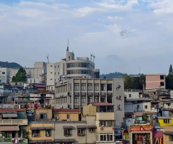 Shapowei,Xiamen,Chinatravel Dense cityscape along a river with colorful storefronts and mid-rise buildings under a blue sky with scattered clouds and birds overhead UX.