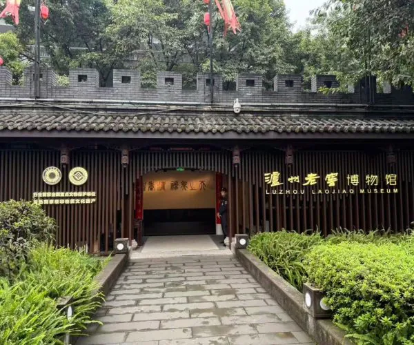 Luzhou Laojiao Distillery Museum,Luzhou,Chinatravel Entrance to Luzhou Laojiao Museum with dark wooden lattice facade, gold signage, and a stone-paved path surrounded by greenery.