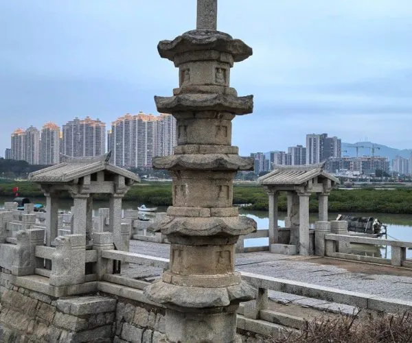 Luoyang Bridge,Quanzhou,Chinatravel Stone multi-tier pagoda and small pavilions on a stone terrace with a river, city skyline in the distance.