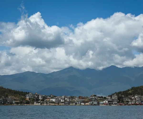 Erhai Lake,Dali,Chinatravel Townside buildings line the lake shore with mountains and blue sky in the distance under fluffy white clouds at midday