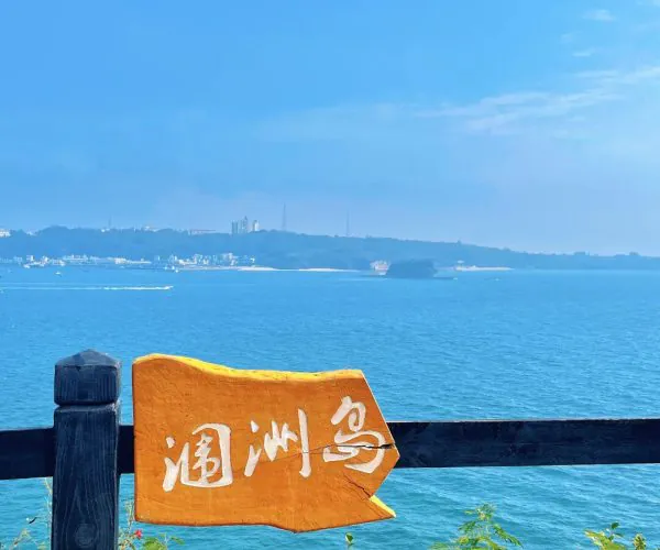 Weizhou Island,Beihai,Chiantravel Weizhou Island,Beihai,Chinatravel Coastal scene with a dark wooden railing, an orange sign with white Chinese characters, and blue ocean beyond.