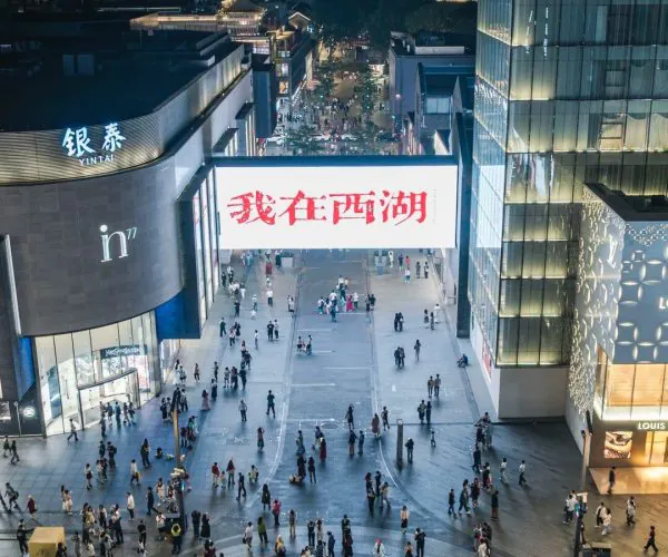 Hubin Shopping District,Hangzhou,Chinatravel Nighttime aerial view of a busy commercial plaza with a large illuminated billboard displaying red Chinese characters over a crowd of shoppers and modern glass buildings.