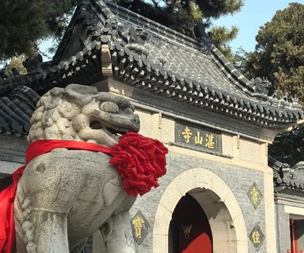 Zhanshan Temple,Qingdao,Chinatravel Stone guardian lion statue wrapped in a red cloth guarding the temple entrance with a curved tiled roof above.