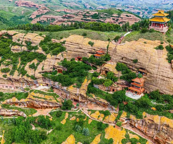 Huoshizhai,Guyuan,China tour Aerial view of a cliffside with red Chinese pagodas and a yellow-roofed temple perched on rugged rock cliffs surrounded by greenery and winding paths.