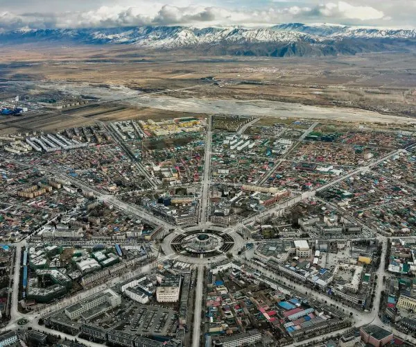 Tekes Bagua City,Ili,China tour Aerial view of a city center with a circular roundabout and radial streets reaching out to dense blocks, mountains in the distance.